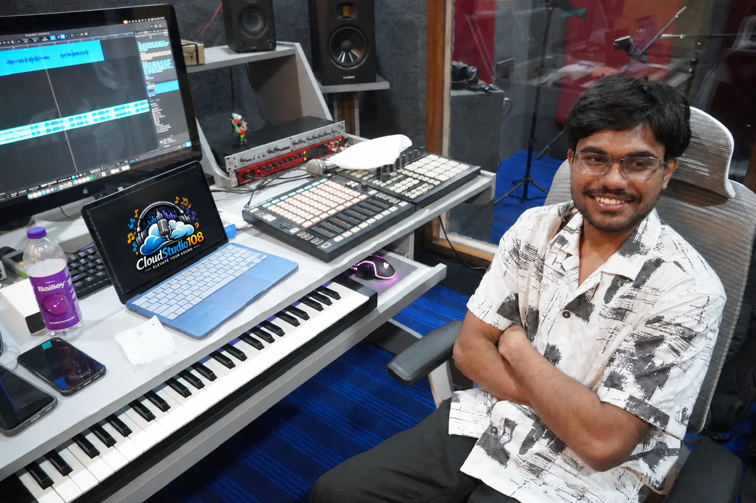 CloudStudio108 sound engineer seated beside the production console with the studio logo displayed on the laptop