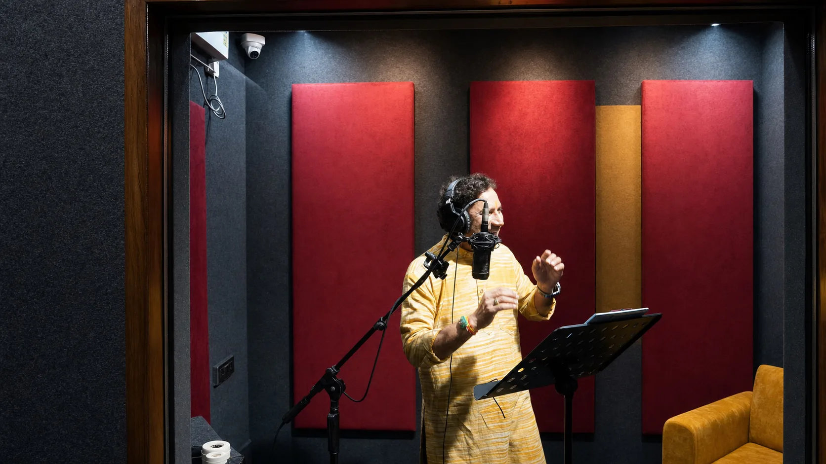 Vocalist in a yellow kurta performing with headphones and a professional studio microphone